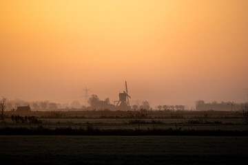 View of a silhouetted windmill standing proudly against a vibrant orange sky, its blades still in the serene landscape, Kockengen, Utrecht, Netherlands.