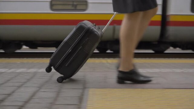 Low section of a woman in motion with a rolling suitcase on a train platform, capturing the essence of travel, commuting, and modern journeys