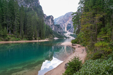 View of turquoise waters mirror the towering mountains and lush forests, a serene landscape blending reflections with the natural beauty, Prags, Trentino-South Tyrol, Italy.