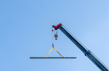 Heavy-duty mobile crane lifting a long steel structural beam high into a clear blue sky.