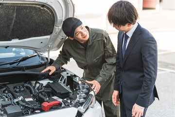 A male mechanic explaining to a driver in a car's engine room
