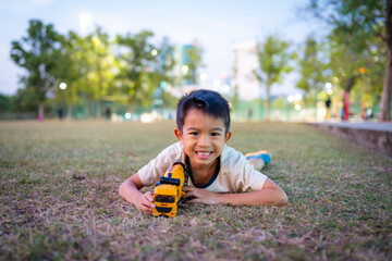 Adorable school boy enjoy truck toy on city park green grass