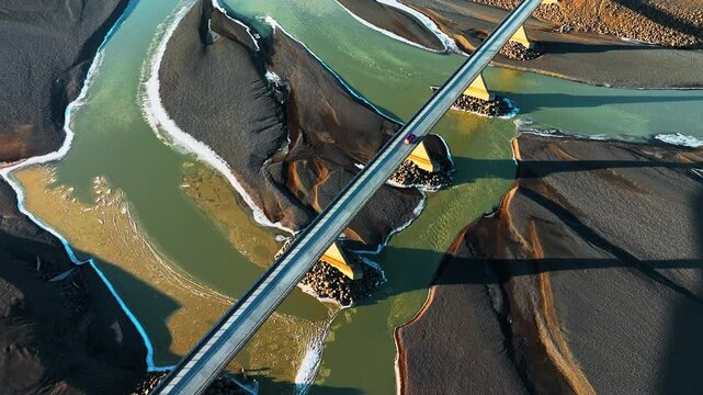 Aerial Drone View of Bridge Crossing Braided River on Dark Volcanic Landscape