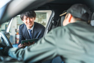 A young Asian businessman in a suit giving instructions to workers in work clothes inside a car
