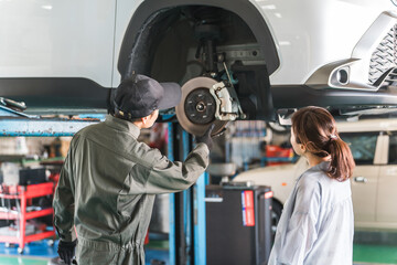 A female customer and a male mechanic receive an explanation about a car that has been lifted for a vehicle inspection
