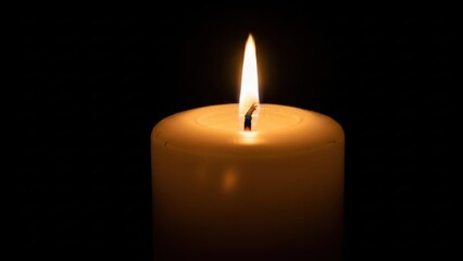 Closeup of a single, thick, white pillar candle burning brightly with a warm, glowing flame against a completely dark, black background, creating a solemn and peaceful atmosphere