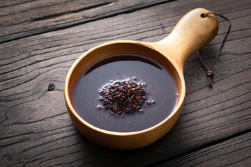 Black rice and rice water are placed in a handmade wooden tray on an old wooden table.	