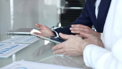 Business partners collaborating on a digital tablet, analyzing financial data and reports during a corporate meeting in a modern office, planning strategies for growth - Powered by Adobe