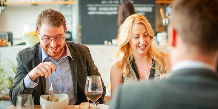 Group dining in a cozy restaurant. Smiling people enjoying a meal. Relaxed atmosphere with wine and conversation. Social dining experience in a cozy setting. Business people out for lunch.