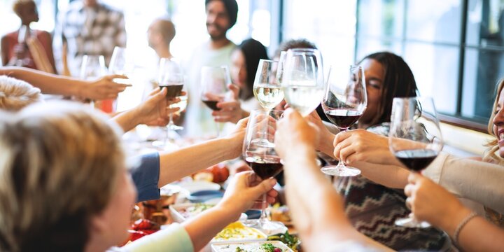 Group of people toasting with wine glasses at a festive gathering. Diverse group enjoying a celebration. Cheers and laughter fill the lively atmosphere. Happy people wining and dining at restaurant. - Powered by Adobe
