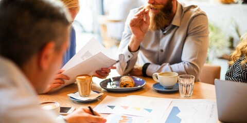 Group meeting with diverse business people discussing charts. Business meeting with charts, coffee, and documents. Professionals collaborating in a meeting. Startup business team working at a cafe.