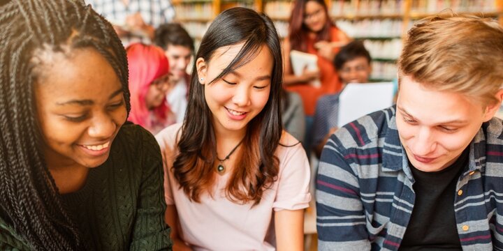 Diverse group of young adults studying together in a library. Smiling students, books, and learning. Multicultural, collaborative, and educational environment. Diverse young people reading at library.
