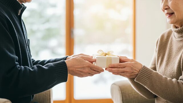 リビングの窓際で、シニアの夫が妻にプレゼントを渡す（手元アップ）