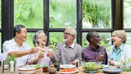 Group of diverse seniors enjoying a meal, laughing and toasting with wine. Happy gathering of elderly friends sharing food and joy around a table. Senior people toasting with wine during lunch.
