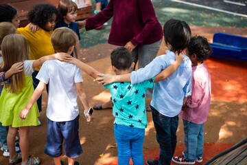 Children in a circle, arms around each other, diverse group, outdoor play, teamwork, unity, diverse...