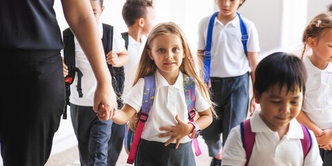 Group of young children with backpacks walking to school. Diverse elementary students walking in school with backpacks. Happy diverse elementary students in school. Diverse kids walking to school.