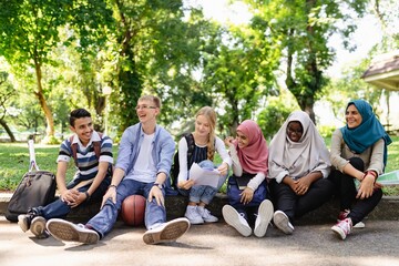Diverse group of young adults sitting outdoors, laughing and chatting. Multicultural friends enjoying time together in a park, showcasing unity and diversity. Diverse young friends in school park.