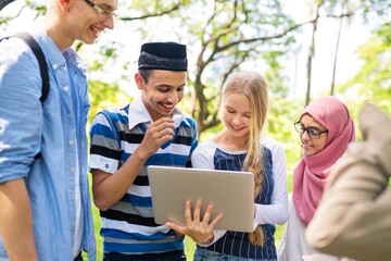 Group of diverse students outdoors, smiling and looking at a laptop. Young people enjoying technology and learning together in a park setting. Diverse students doing homework together.