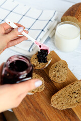 Slices of homemade bread topped with dark berry jam on a wooden board, served with milk. Bright kitchen setup styled in a cozy, homemade breakfast mood.