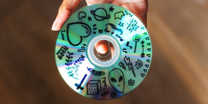 Hand holding a retro CD with doodles. CD features doodles of hearts, aliens, and stars. Creative CD design with playful doodles. Unique CD art with various doodles.