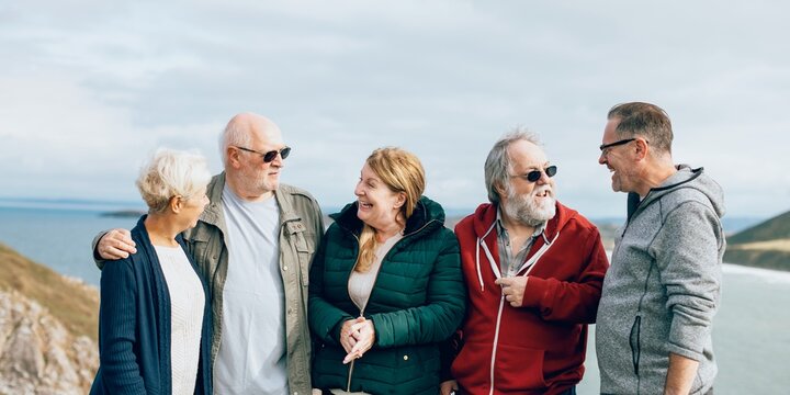 Group of elderly friends, men and women, stand together by the coast. Senior friends embrace, Elderly friends share moments at the coast. outdoor nature. Elderly friends have good time at coast