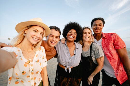 Group of friends taking a selfie on the beach. Diverse group smiling, enjoying the beach. Happy friends, beach vibes, diverse group, fun times. Diverse happy adult friend group photography.
