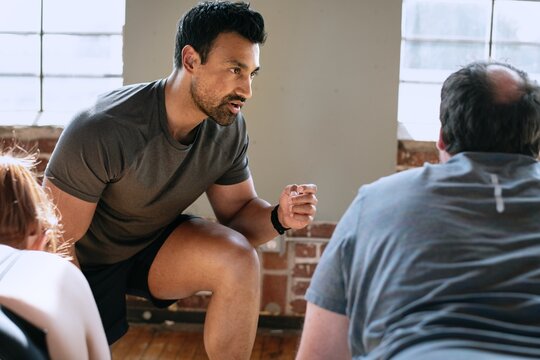 Male fitness trainer, instructing a group workout. The fitness trainer, focused and energetic, guides participants. Male fitness trainer in fitness, training session in gym