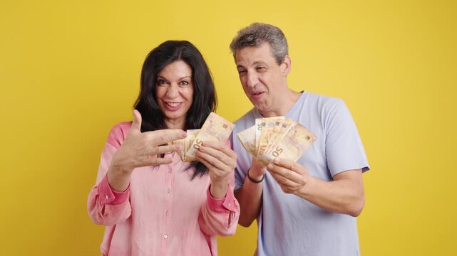 Joyful middle-aged man and woman showing off wads of euro banknotes. Their excited expressions convey success, wealth, and winning a prize