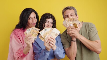 Joyful family celebrating a lottery win. Excited mother, father, and daughter holding and waving wads of cash on a yellow background