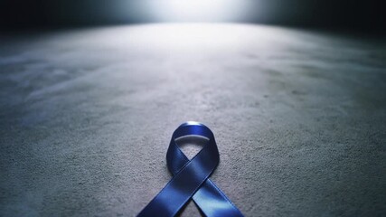 A single dark blue awareness ribbon lies on a textured concrete surface with dramatic lighting.