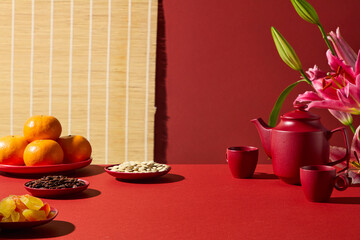 Lunar New Year themed setup with a red tea set, decorative flowers, fruits, and traditional red background. Space for product placement, New Year promotions, advertising layouts, and design