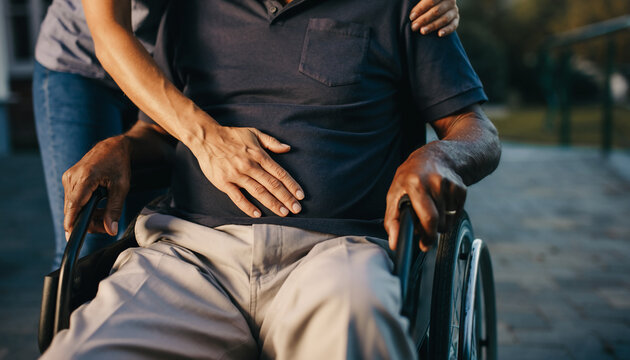 Compassionate caregiver providing comfort and physical support to an elderly disabled man sitting in a wheelchair outdoors during the day