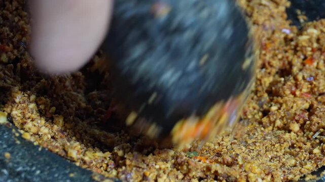 Homemade peanut chili sauce being ground in a stone mortar. Traditional Indonesian sambal making process closeup