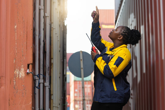Female inspector checking cargo containers at shipping yard, Logistics worker using walkie talkie for container inspection, Warehouse staff monitoring safety and operations in container terminal