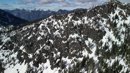 Aerial vertical footage capturing a frozen alpine lake surrounded by snow-covered mountains and evergreen forest in the Cascade Range, Washington State. - Powered by Adobe