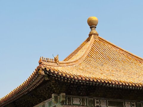 Traditional Chinese architecture roof detail with yellow glazed tiles and ornate eaves against a clear blue sky. - Powered by Adobe
