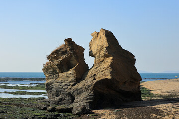 Scenic coastal landscape featuring a prominent sea stack rock on a sandy shore during low tide.