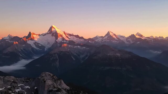 Majestic, snow capped mountain range at sunrise, with deep valleys filled with ethereal mist and golden light illuminating rugged peaks. Wide aerial shot slowly panning across the vast wilderness.