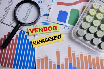 Concept of vendor management write on sticky notes with financial graphs isolated on Wooden Table.