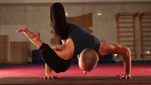 Male yogi practices Eka Pada Koundinyasana II in gym hall showcasing dedication to physical and mental balance. Healthy concept living motivation achieving fitness goals through advanced yoga HD video