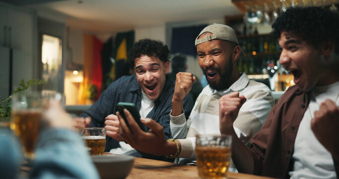 Phone, cheering and friends in pub for sports game with goal, victory or winning championship. Happy, cellphone and group of male fans with celebration for watching football match in bar together.