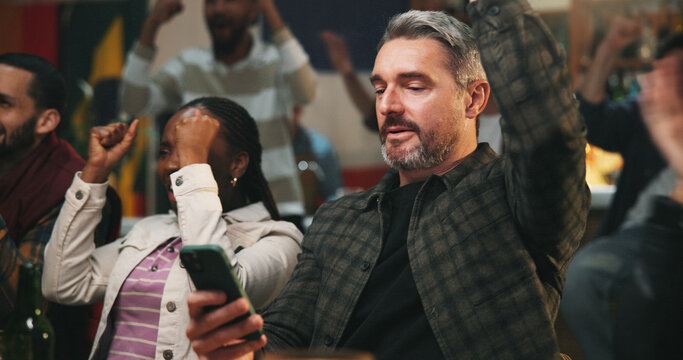 Winning, man and celebration with phone in pub for streaming match, sports goal or team support. Football fans, mature person or mobile app in bar for online game score, live results or viewing party