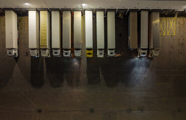 Aerial view captures a row of freight trucks parked at a loading dock under dim overhead lights.