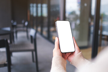 Mockup image of a woman holding and using mobile phone with blank desktop screen in cafe