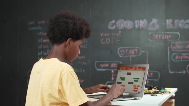 Back view of african boy programming system or coding system. Professional high school student working learning to write engineering code while sitting blackboard. Creative education. Edification