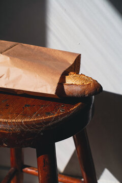 Close-up of crusty baguette in kraft paper bag on vintage stool
