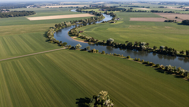 Aerial view of a winding river flowing through lush green agricultural fields under a bright summer sky - Powered by Adobe