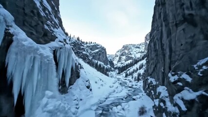Aerial view of a narrow, snowcovered canyon with a partially frozen river flowing between steep rock walls - Powered by Adobe