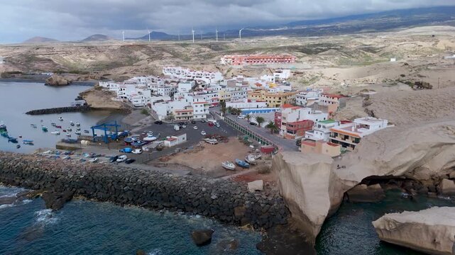 Aerial drone shot panning up and out, revealing the colorful fishing harbor and houses of San Miguel de Tajao, Tenerife, Canary Islands, Spain.