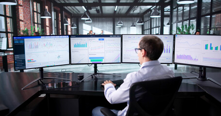 Man Managing Financial Analytics Data On Multiple Computer Monitors In Office